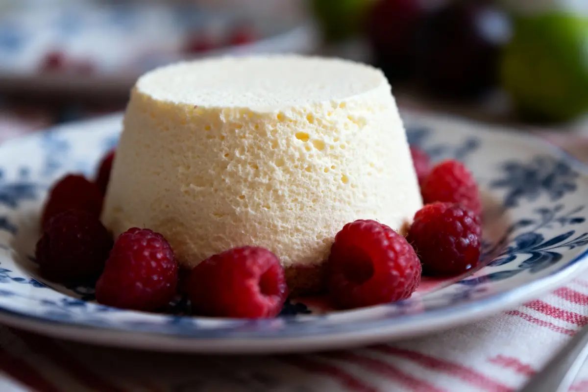 Dessert crémeux blanc avec framboises fraîches, présenté sur une assiette décorative bleue et blanche.