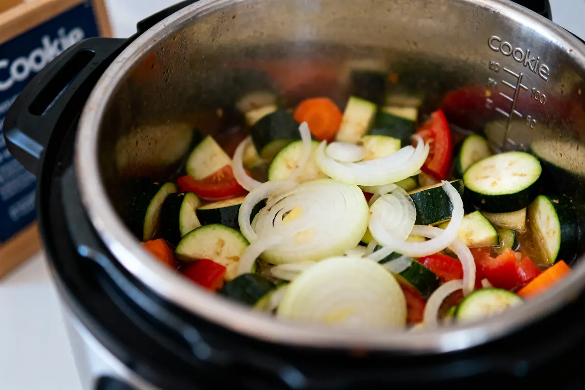 pexels-michal-pech-213601-757318 (1) Légumes frais coupés en tranches, courgettes, tomates, oignons dans une cocotte-minute en acier inoxydable.