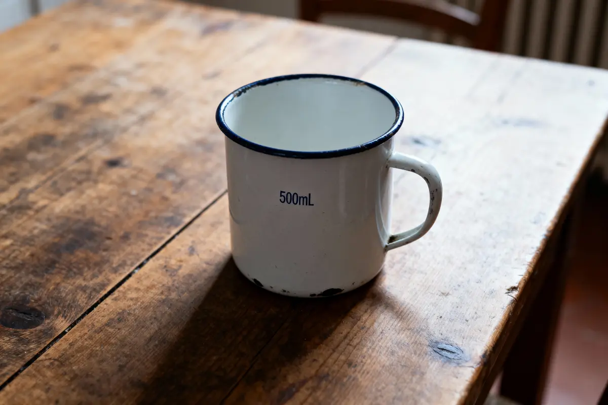 Tasse en métal émaillé blanc, 500 mL, sur une table en bois rustique.