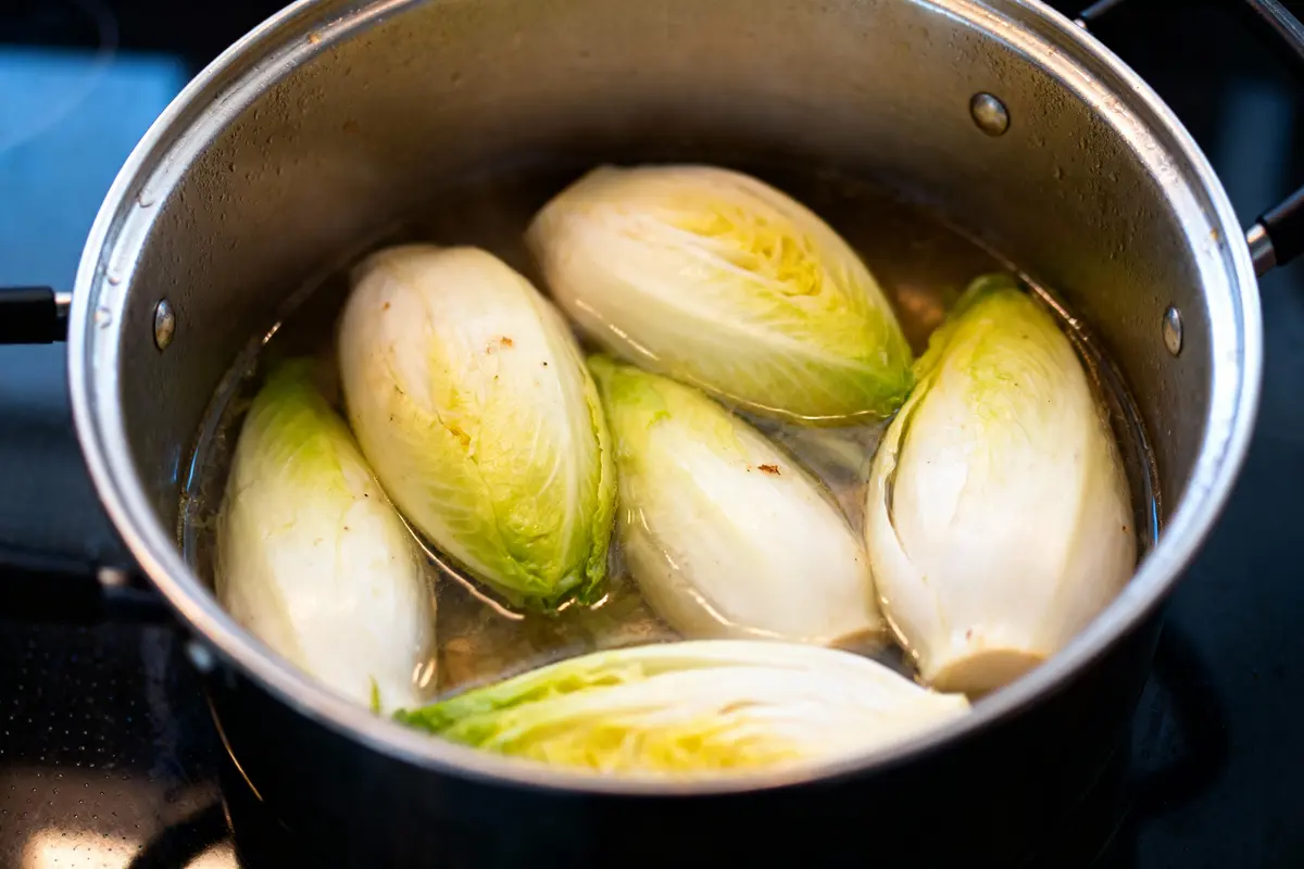Endives crues blanchies dans une casserole d'eau bouillante sur la cuisinière.