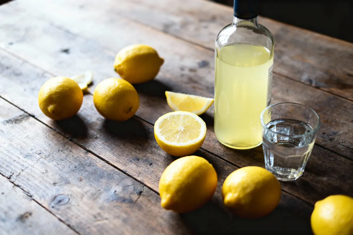 Bouteille de limonade, citron coupé, citrons entiers et verre d'eau sur table en bois rustique.