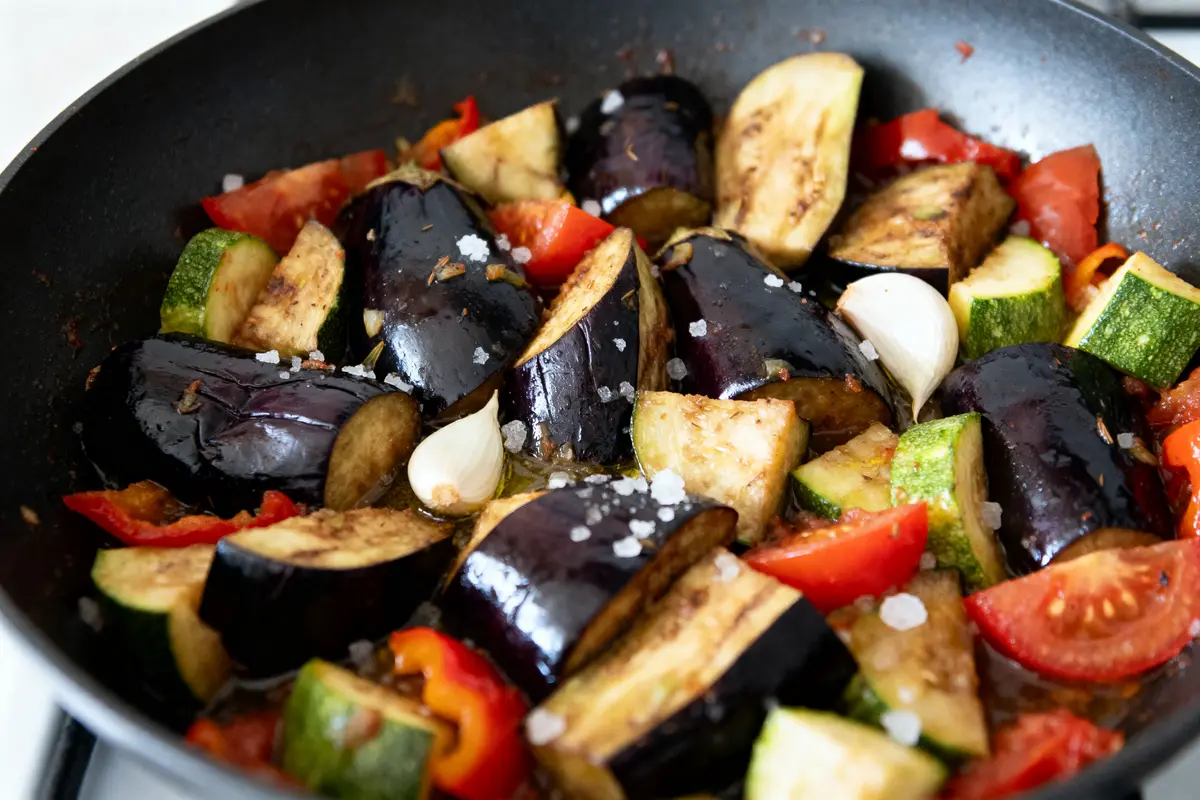 Légumes sautés assortis dans une poêle: courgettes, aubergines, tomates, ail, et gros sel.