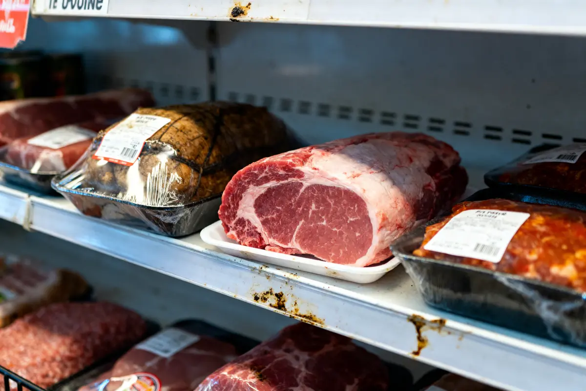 Morçeaux de viande emballés et non emballés dans un réfrigérateur de supermarché sur des étagères.