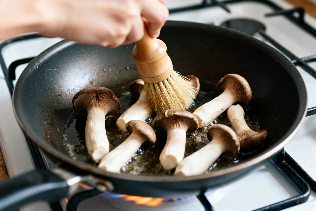 Cuisson de trompettes-de-la-mort sur une poêle avec brosse en bois.
